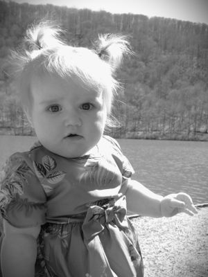 Black and white portrait of a toddler in a dress by a lake.