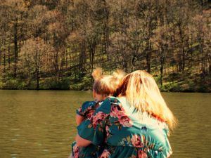 Two people in matching floral dresses look out over a peaceful lake.