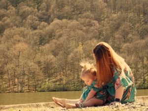 Two people in matching dresses sit together on the shore of a lake.