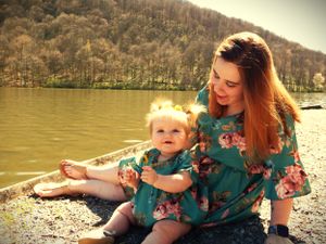 Two people in matching teal floral dresses share a moment by the water.