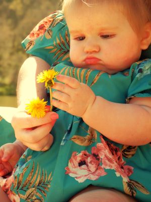 Close-up sequence of a young child in teal floral clothing examining a yellow dandelion flower.