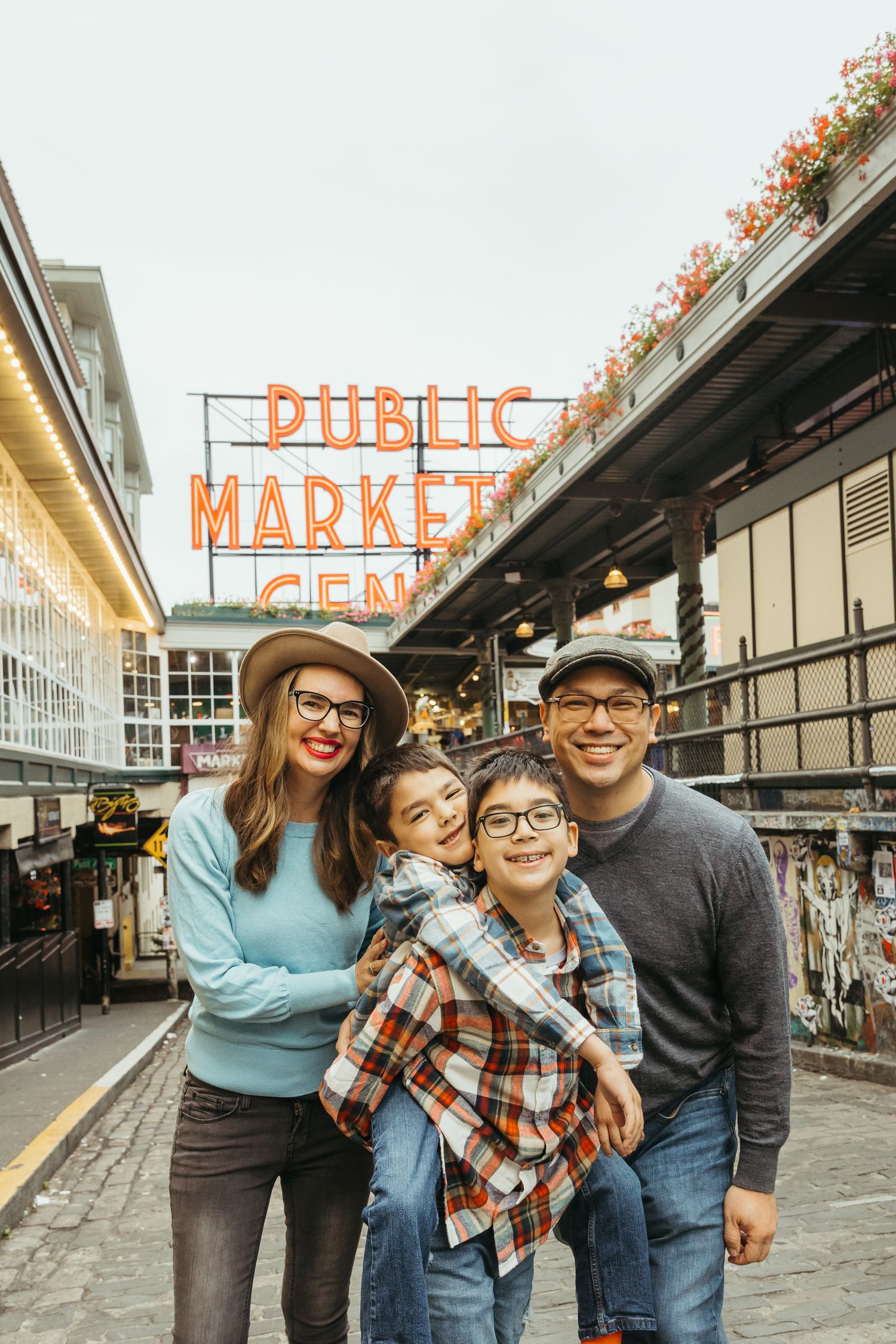 Family poses together at Pike Place Market in Seattle with iconic orange sign visible in background.