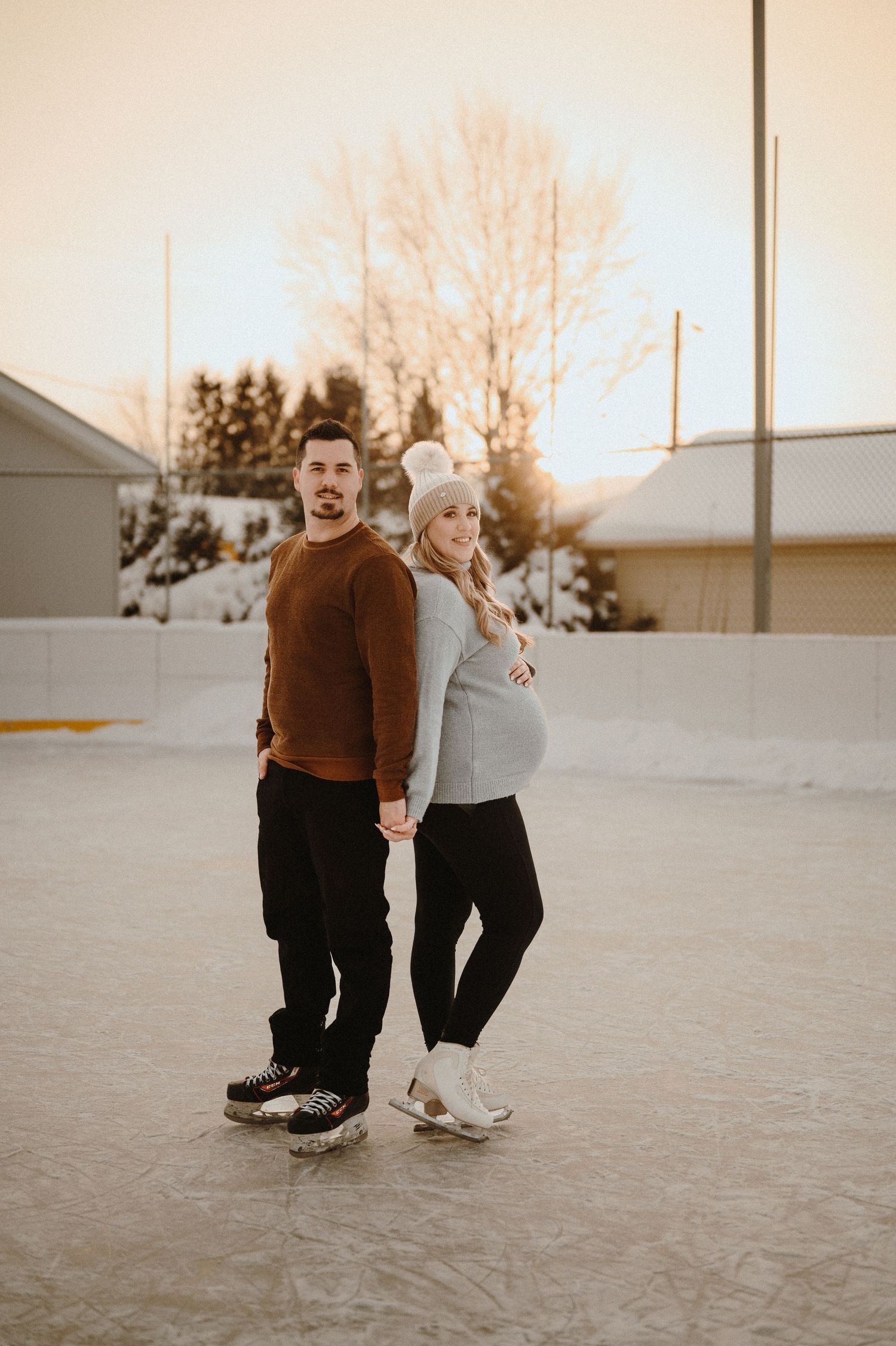 A couple stands back-to-back on an outdoor ice rink during winter.