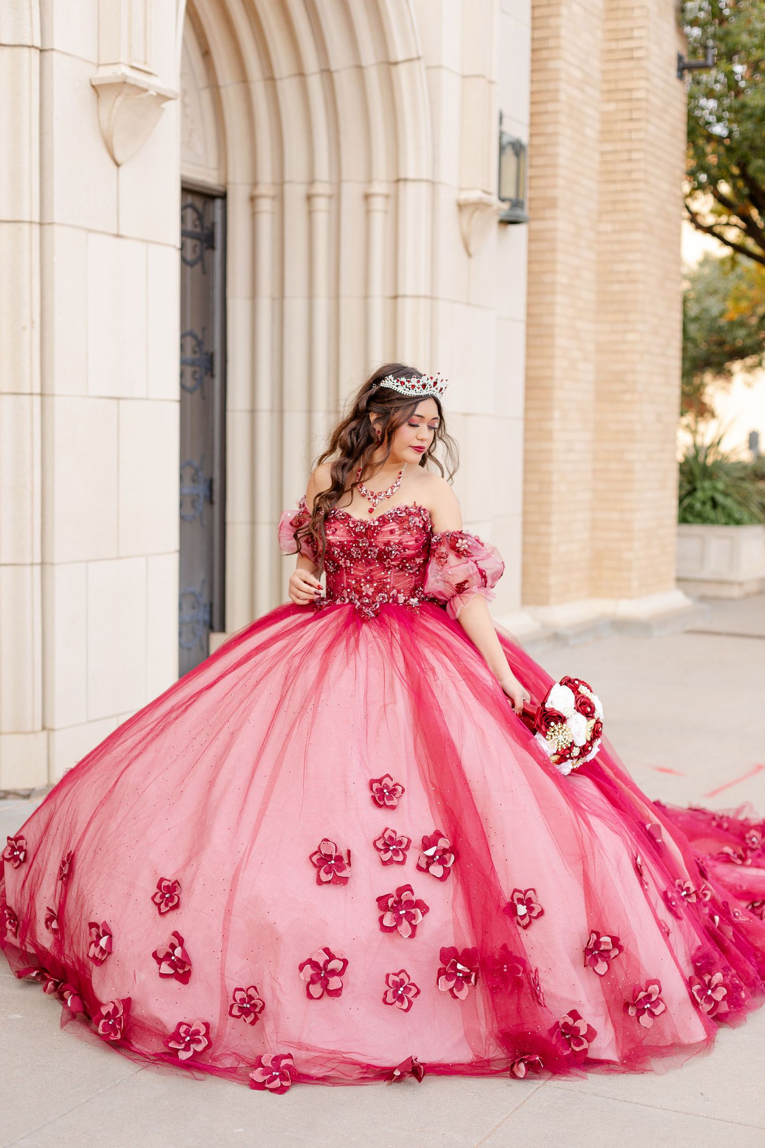 Stunning pink quinceañera ball gown with floral appliques and off-shoulder design in an elegant archway.