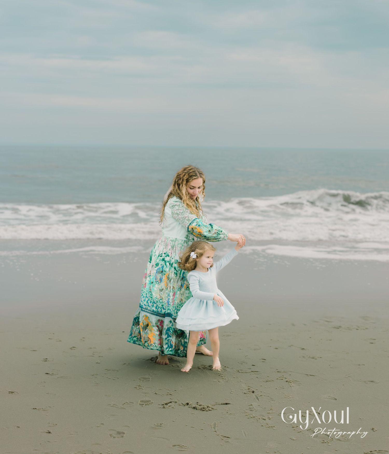 A tender moment captured on a misty beach as they dance together in floral dress and white dress near the ocean waves.