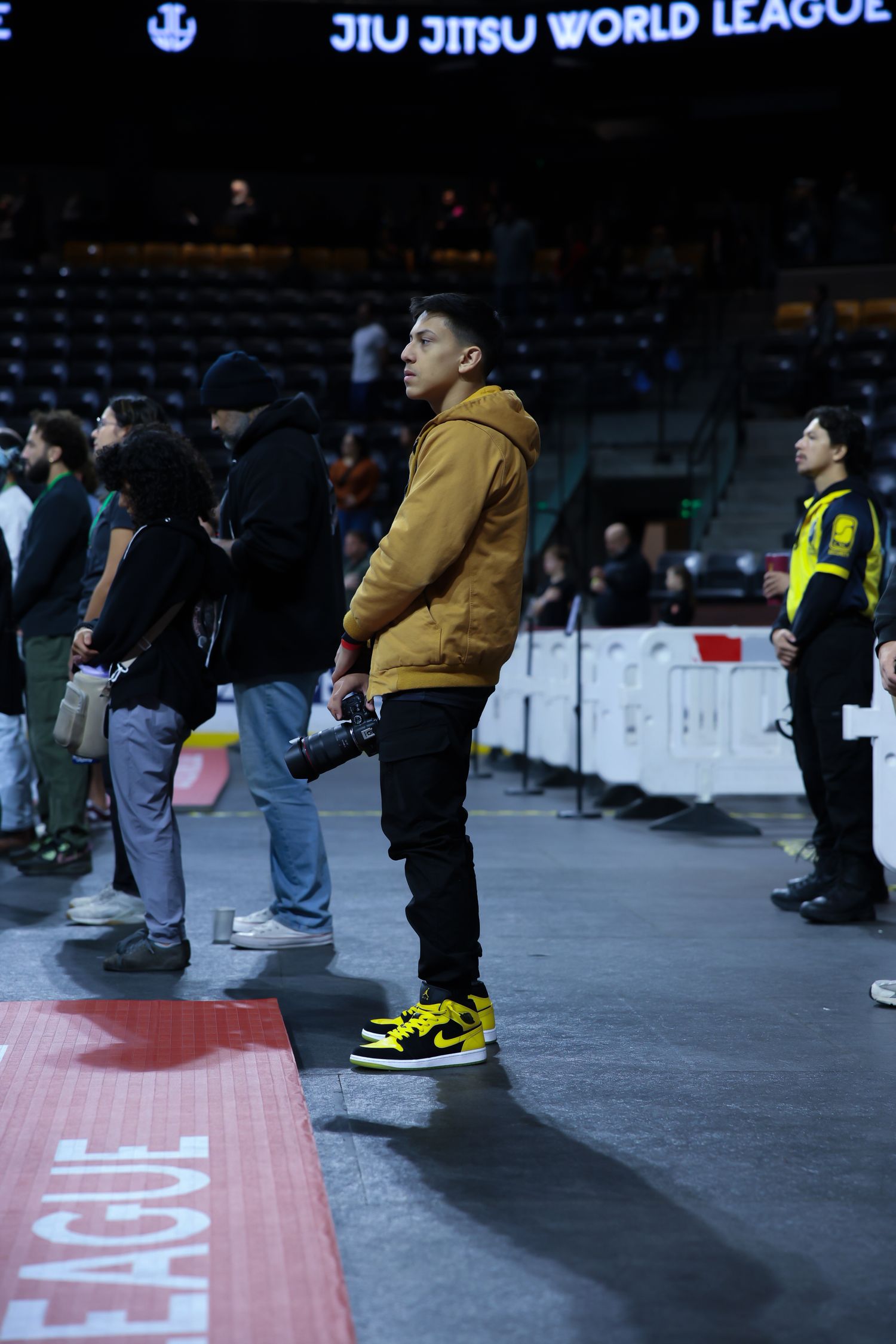 Spectators lined up along the edge of a competition area at a jiu-jitsu tournament.
