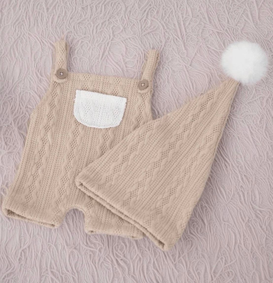 Beige quilted baby romper with white pocket accent displayed on textured background.