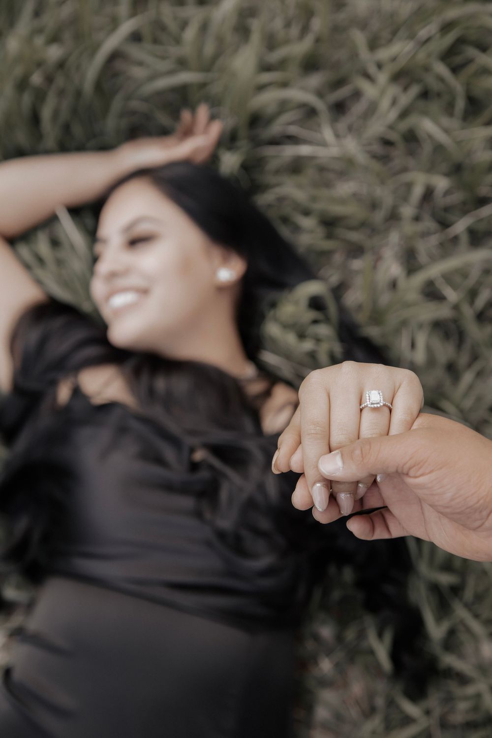 Woman laying in the grass showing off engagement ring