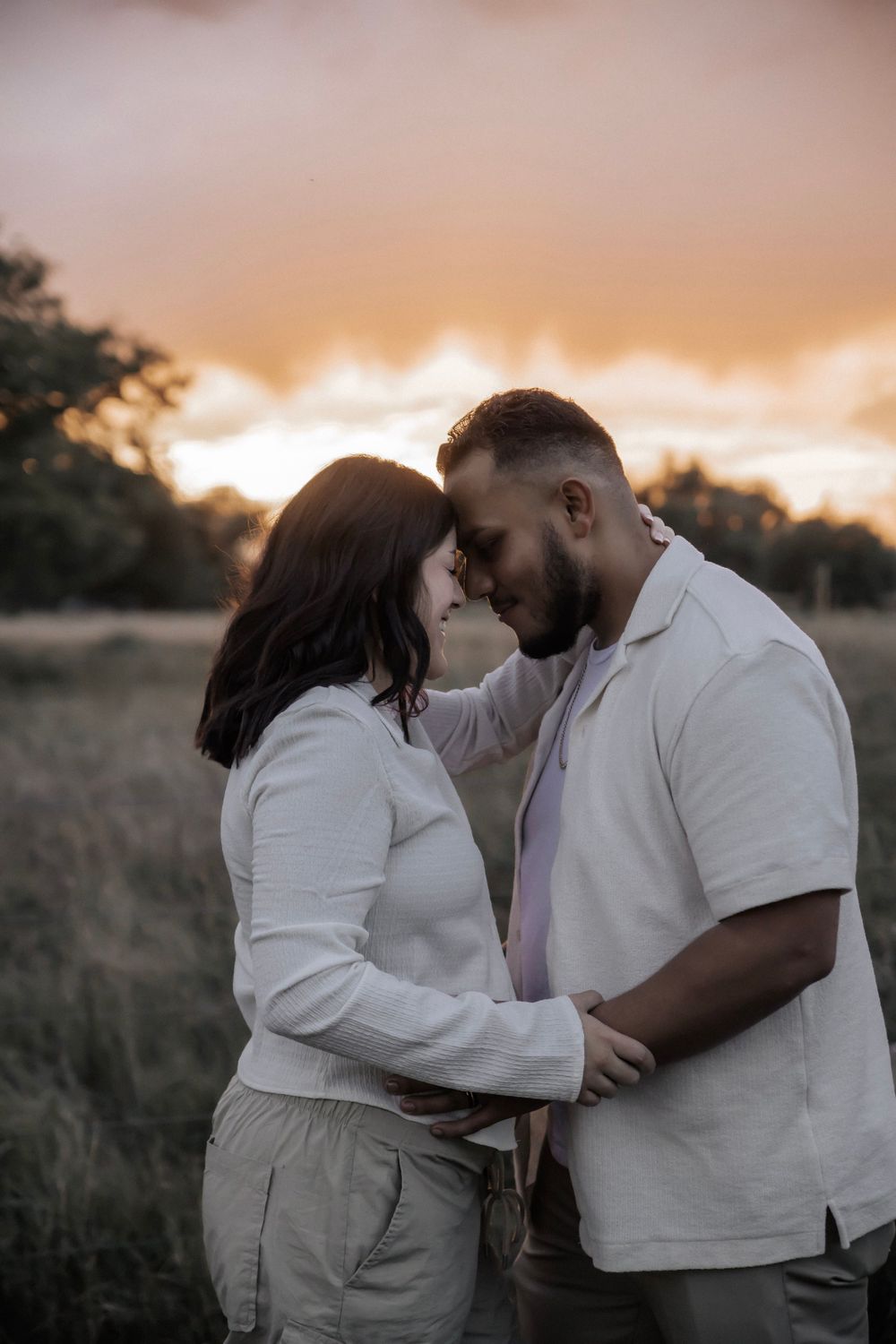 Couple standing with foreheads together as the sun is setting in the background