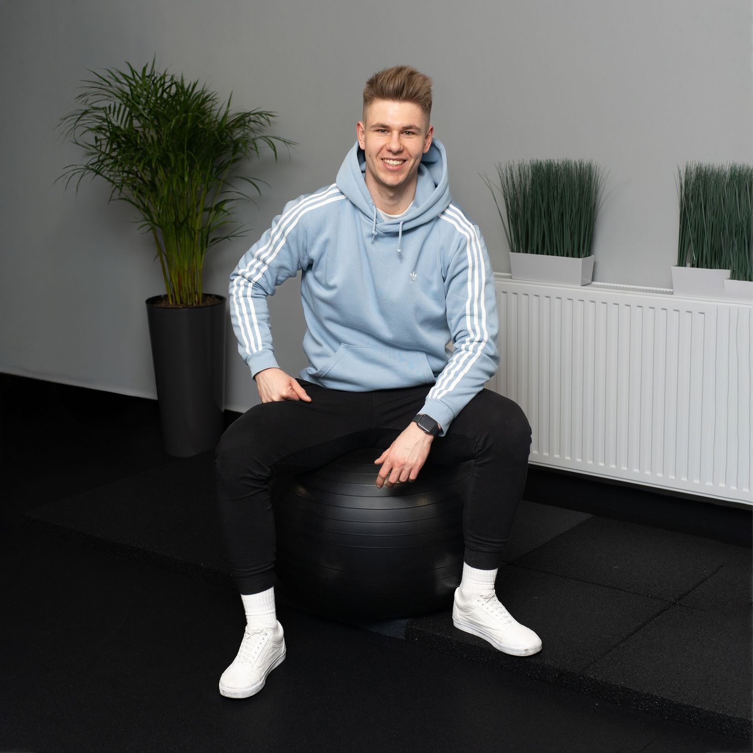 Fitness trainer sitting on exercise ball in modern gym studio with plants.