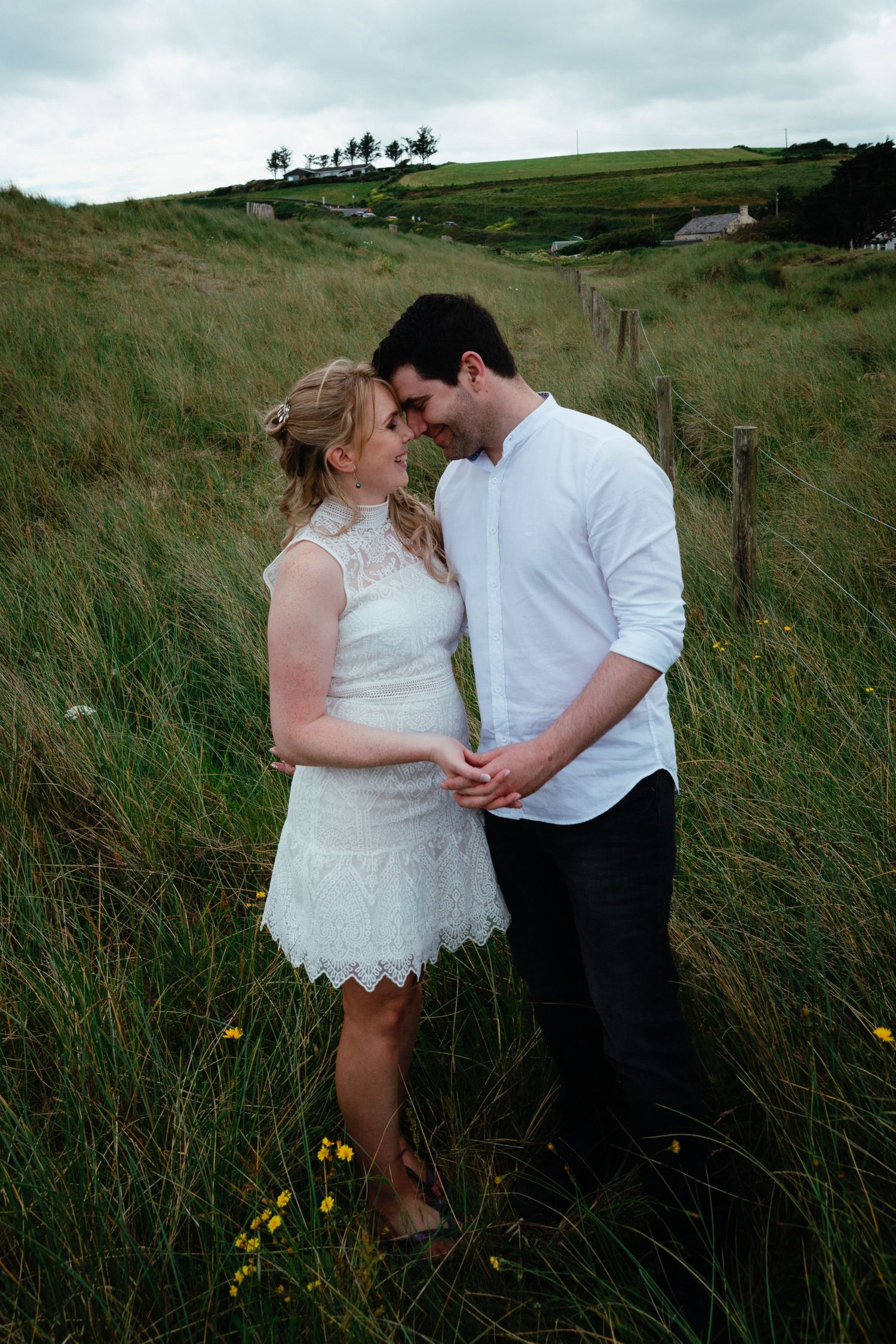 Couple shares romantic moment together in grassy countryside hills at dusk.