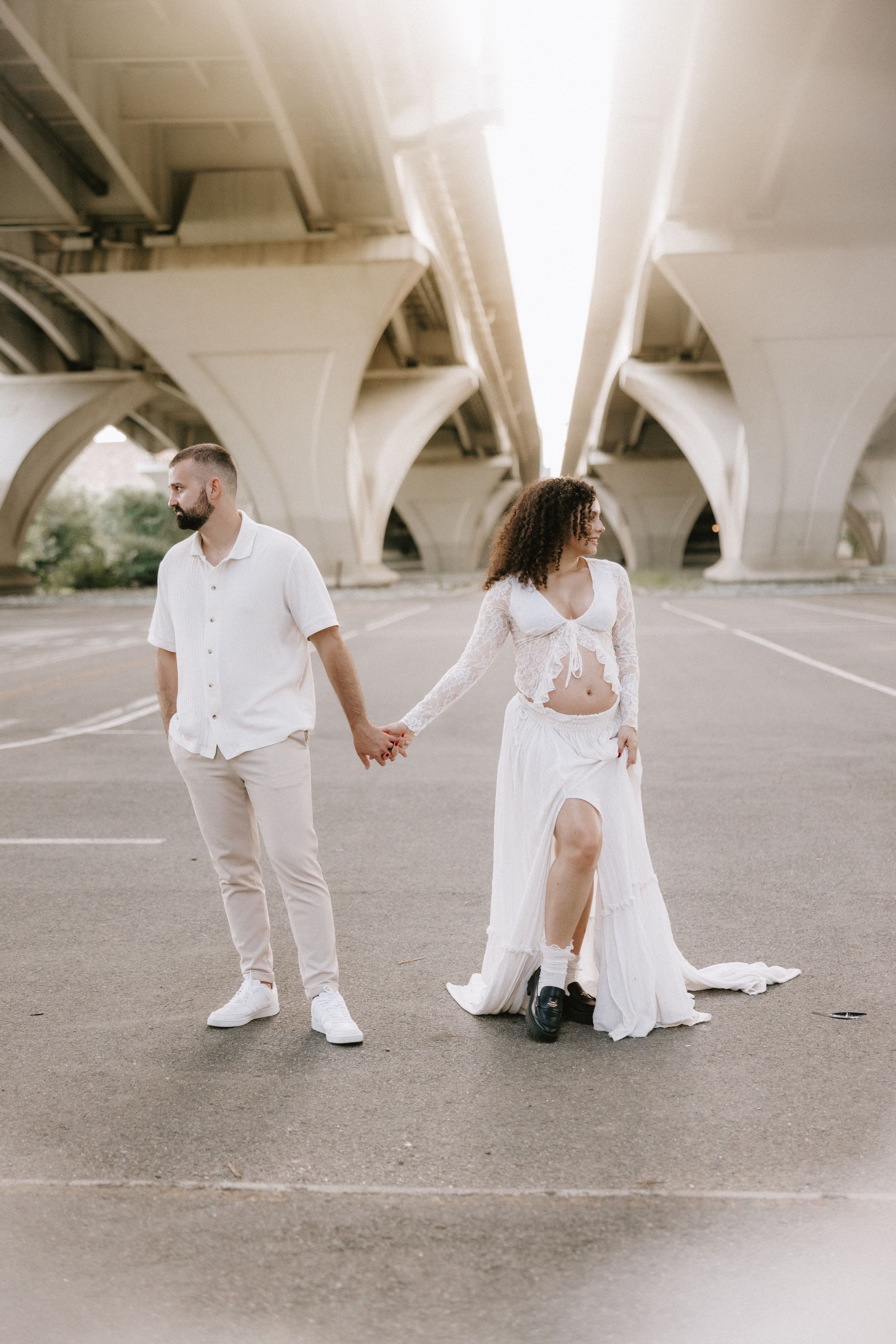 A couple in white outfits poses playfully in a concrete parking structure, creating a series of artistic romantic shots.