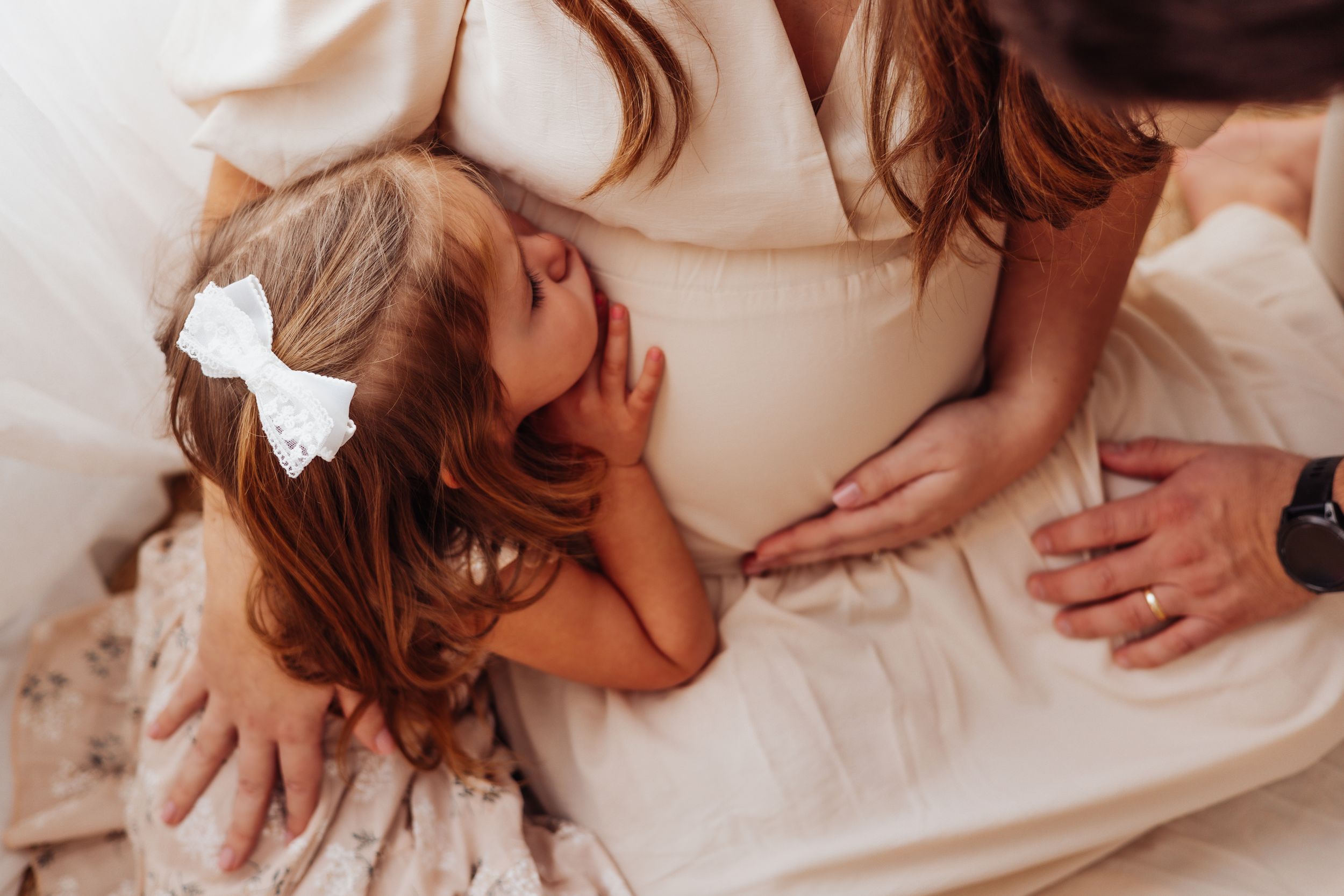 A tender moment captured during bedtime as hands gently comfort a child with a white bow in their hair.