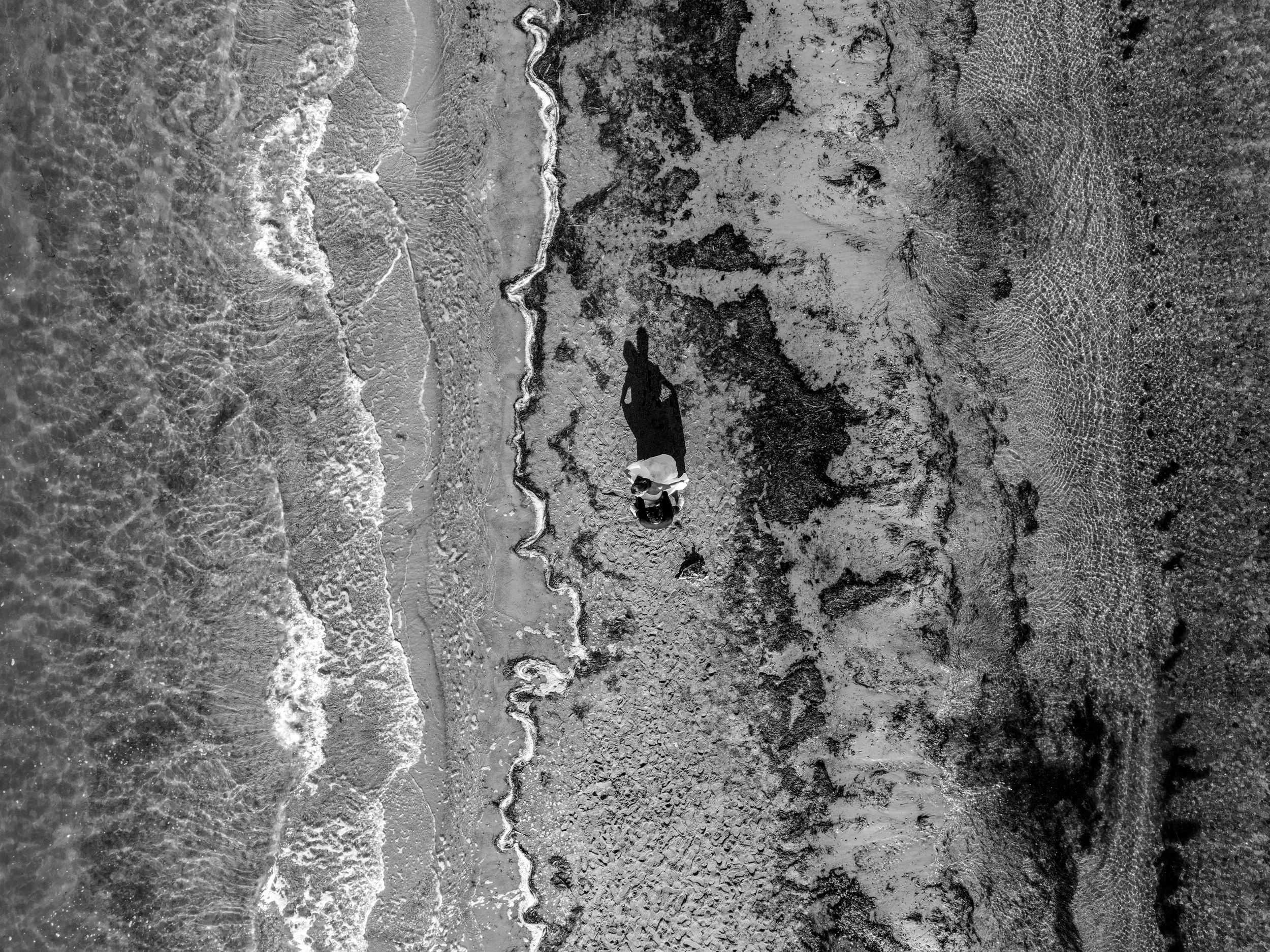 Black and white aerial view shows rugged coastal patterns with waves meeting weathered cliffs and rocky beaches.