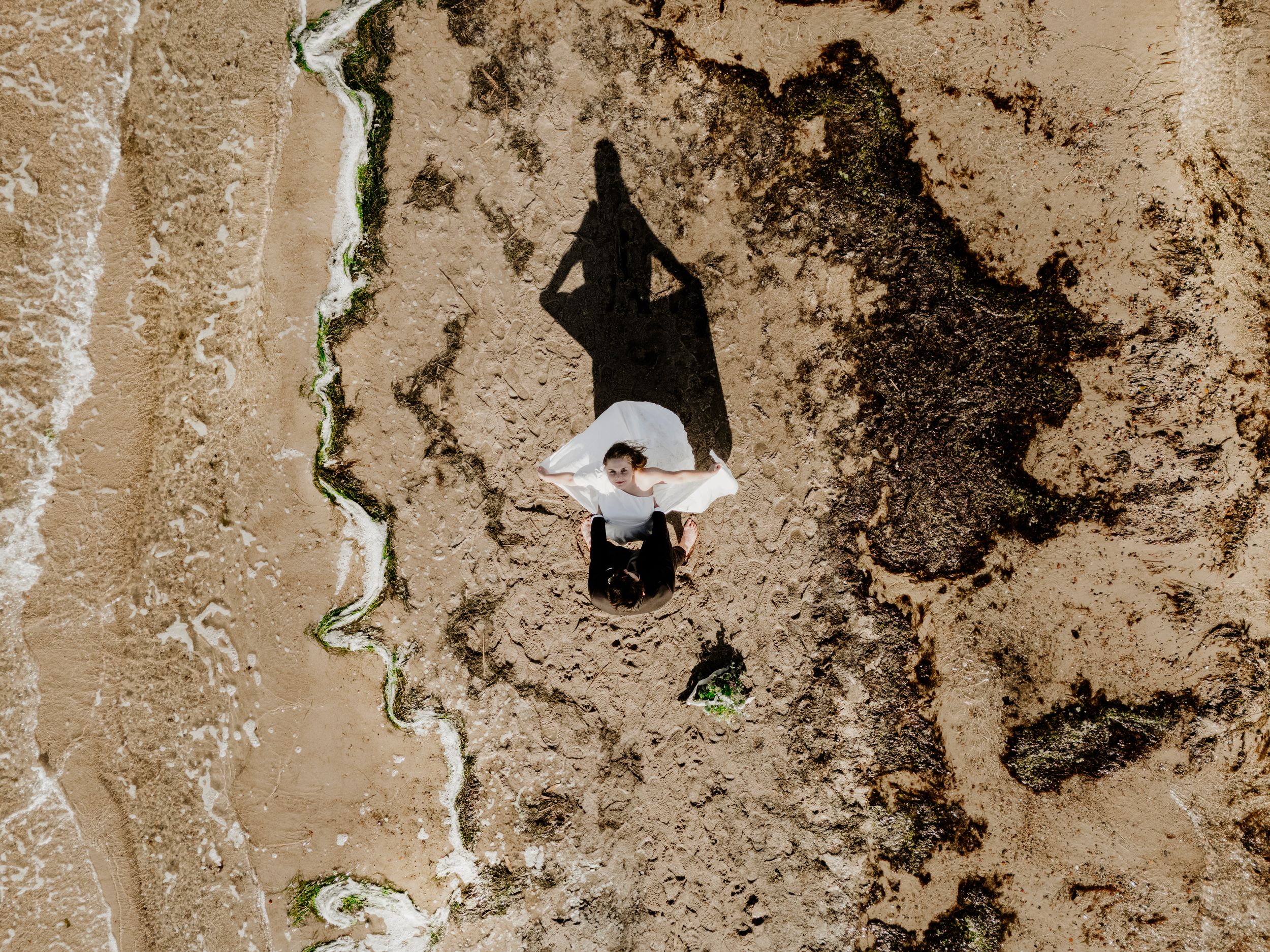 Aerial view of someone in a white hat creating a dramatic shadow on sandy beach terrain.