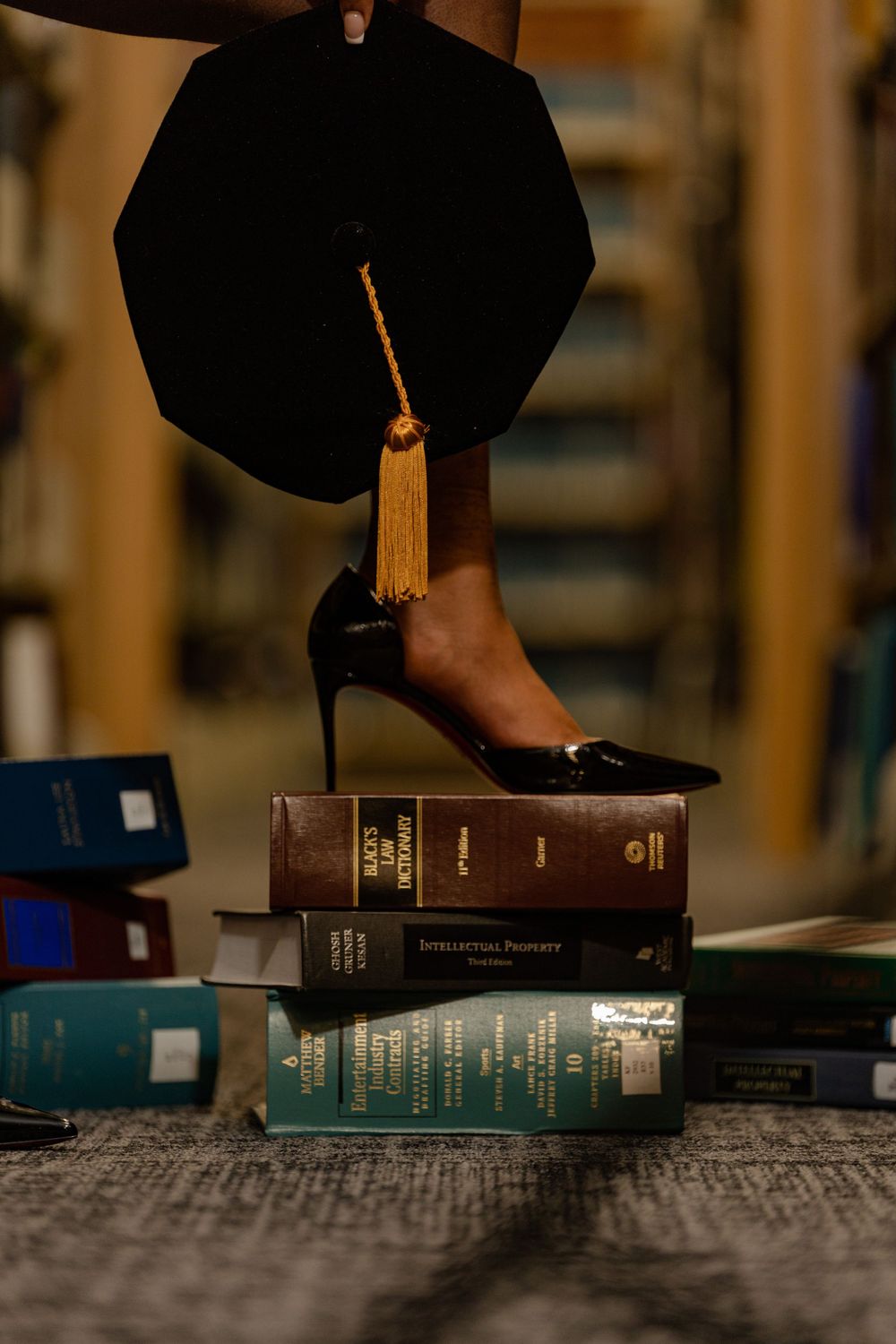 A graduation cap and shoe rests on top of a stack of books against a blurred background.