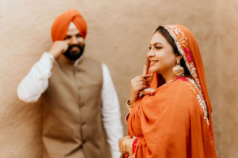 Traditional Punjabi couple in wedding attire poses against beige wall with orange and brown color palette.