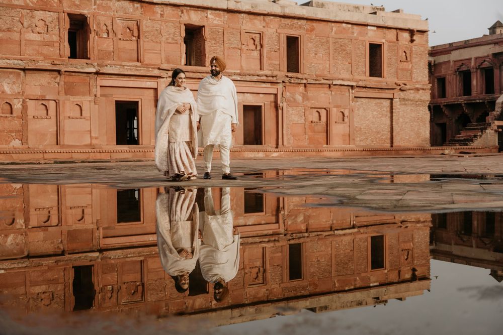 A traditional South Asian couple stands by a reflective pool outside an ancient brick building in Lahore Fort, Pakistan.