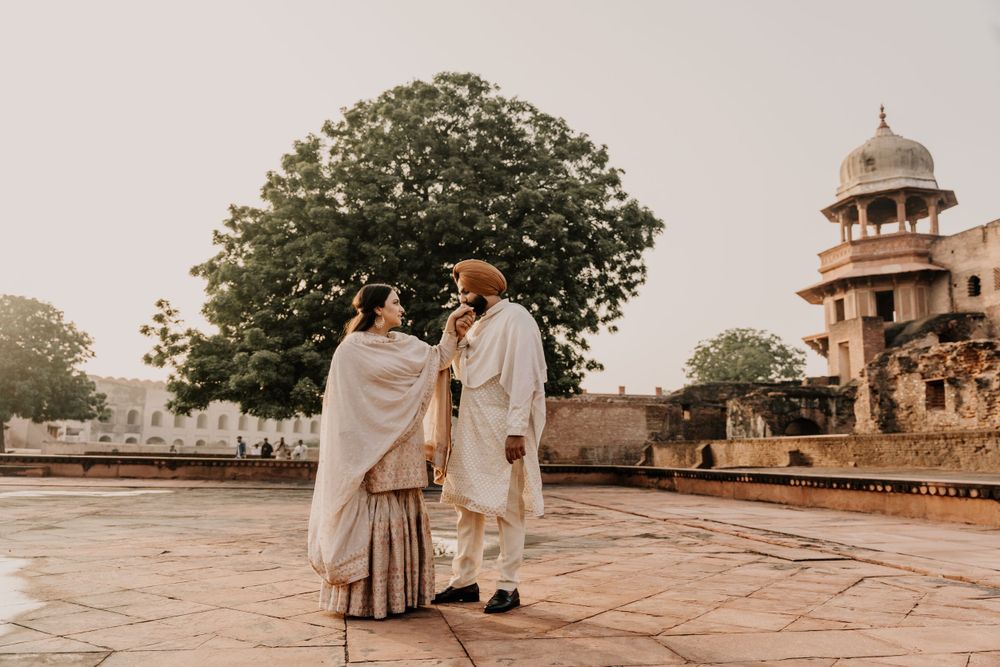 Two people in traditional Indian attire conversing in a courtyard with historic architecture and a minaret tower in the background.