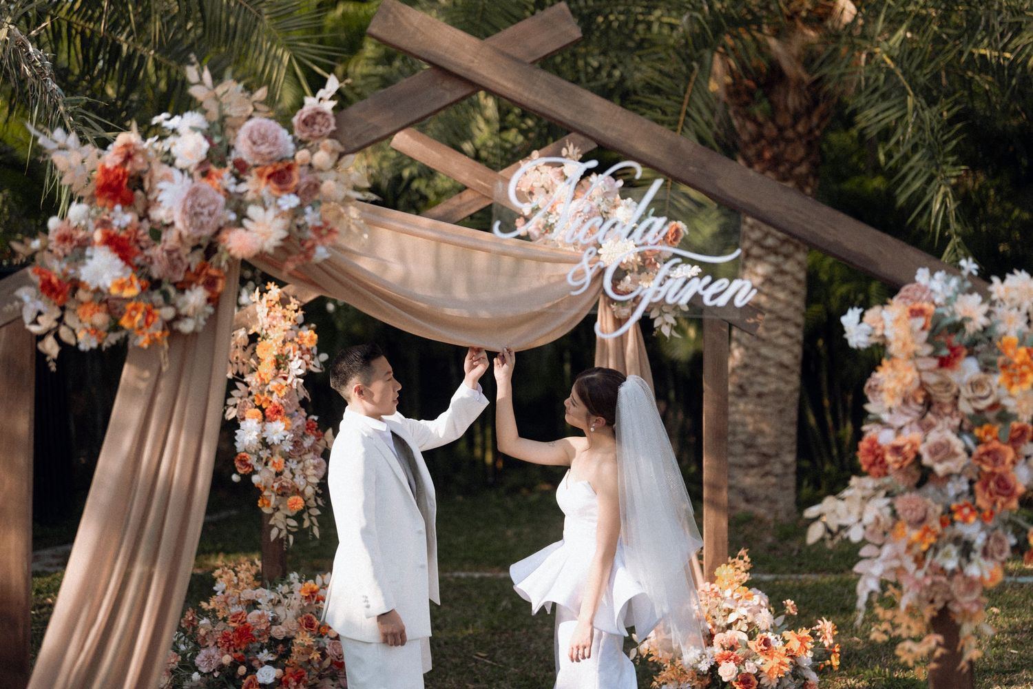 Wedding ceremony under floral arch with peach and white blooms and draped fabric.