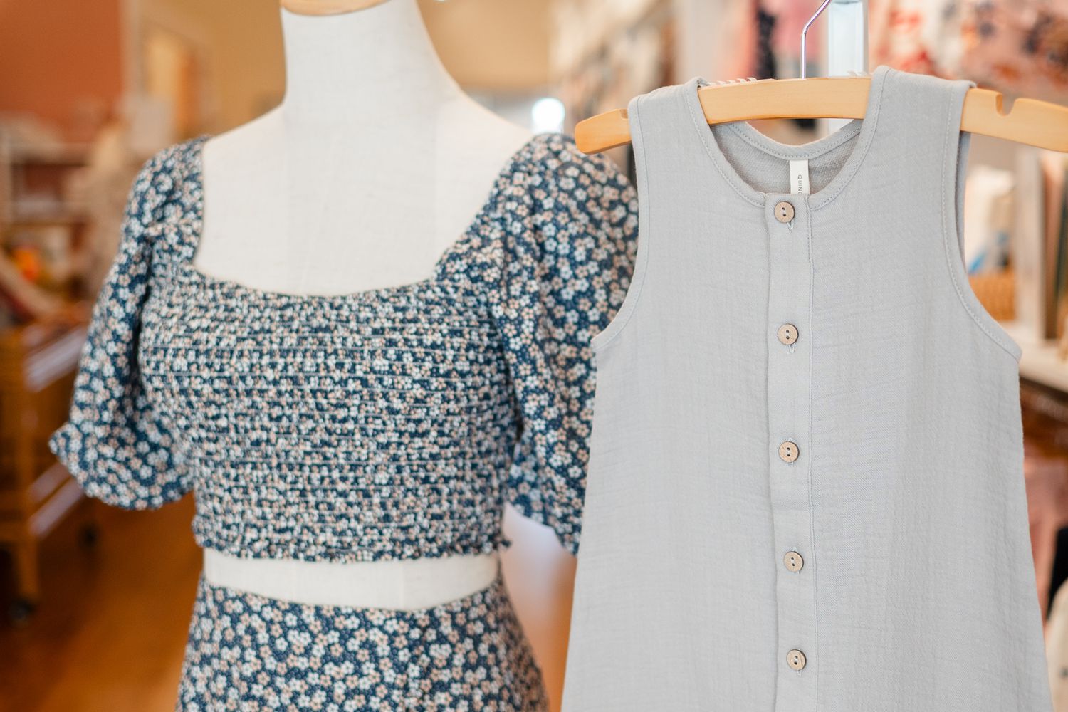 Two summer dresses on display, one blue floral with puff sleeves and one light gray button-front dress.
