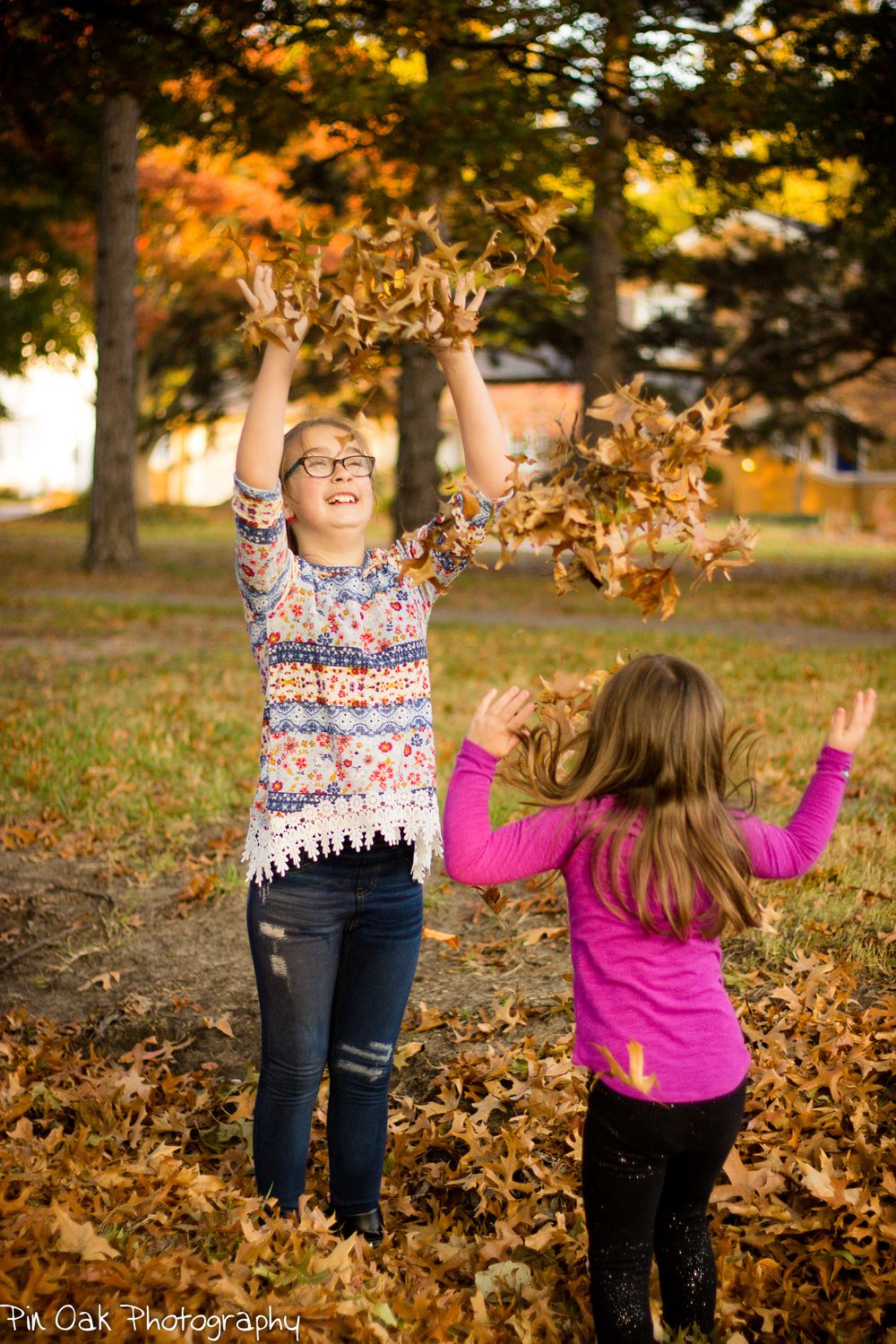 Children playing in and throwing fall leaves at the park.
