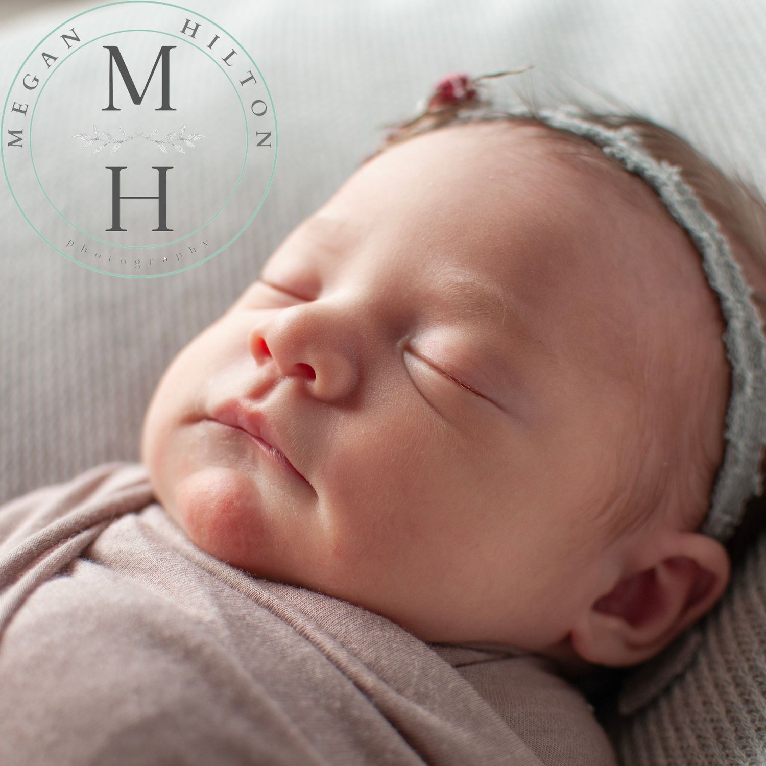 A close up image of a sleeping newborn baby wearing a delicate lace headband and wrapped in soft gray fabric.