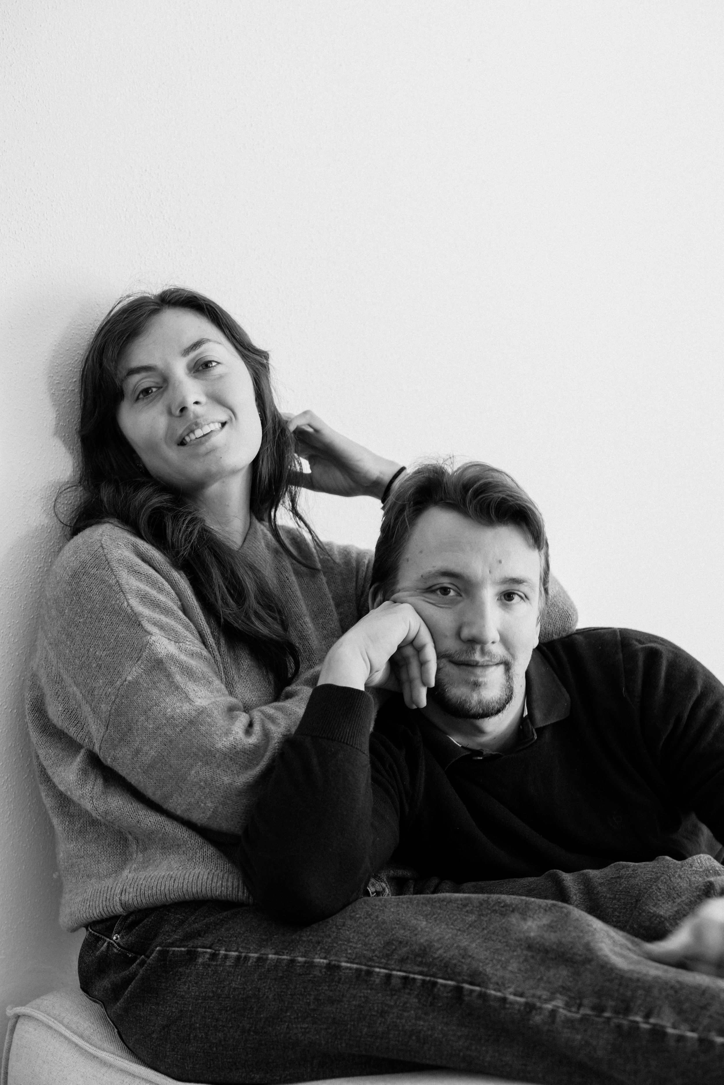 Couple relaxing together in casual attire against white background in black and white photography.