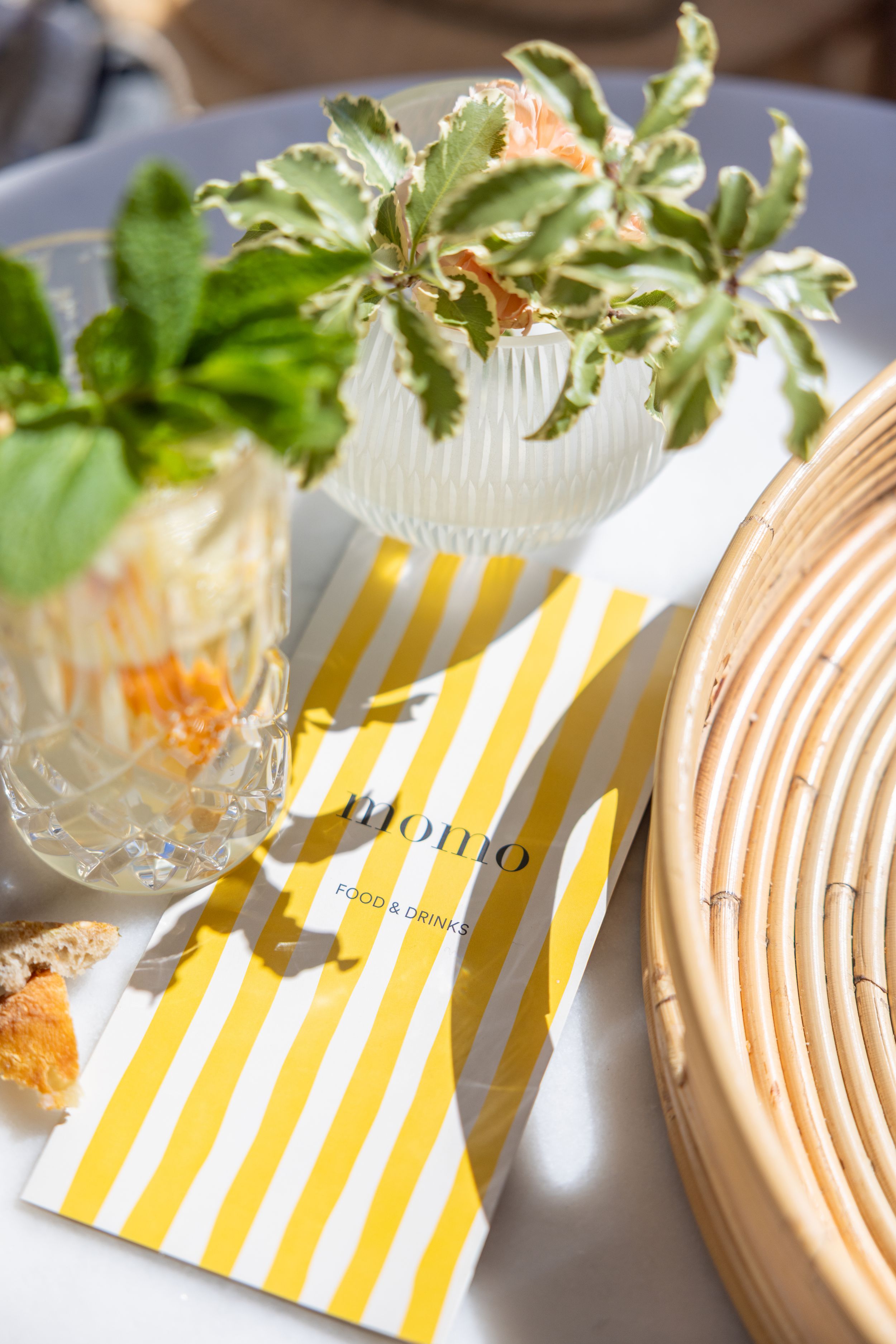 Table setting with yellow striped napkin, potted plant and glassware on elegant dining surface.