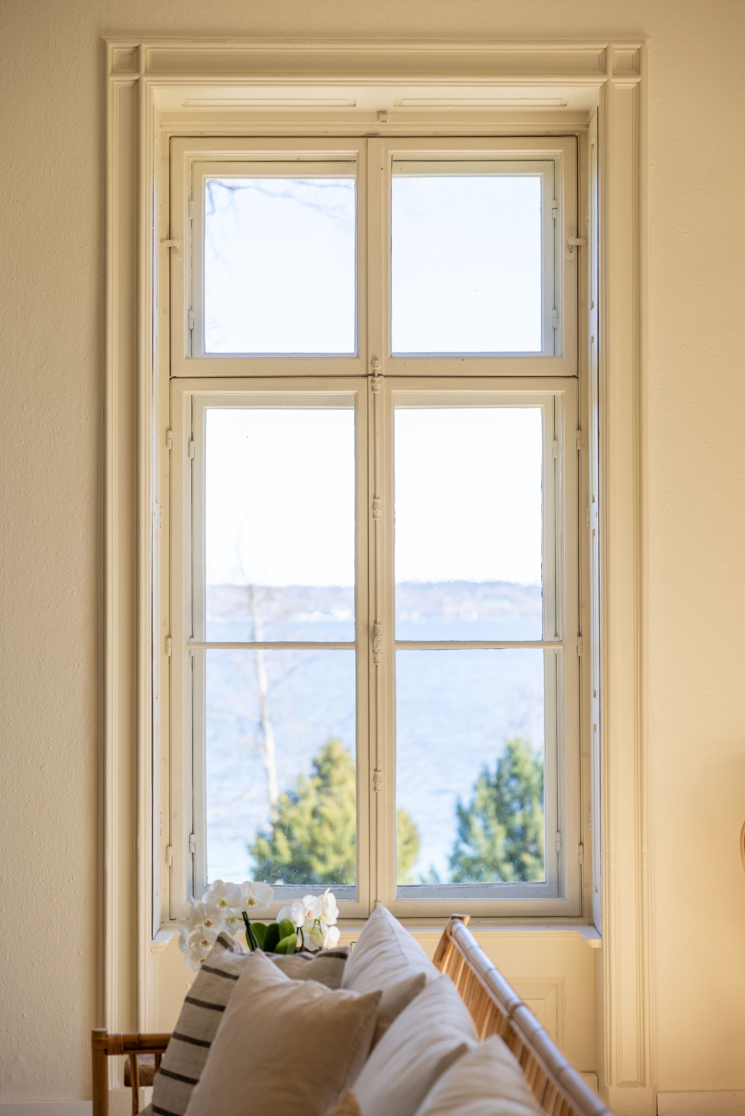 Tall window with white trim overlooking mountains and trees, with cozy pillows on the windowsill.