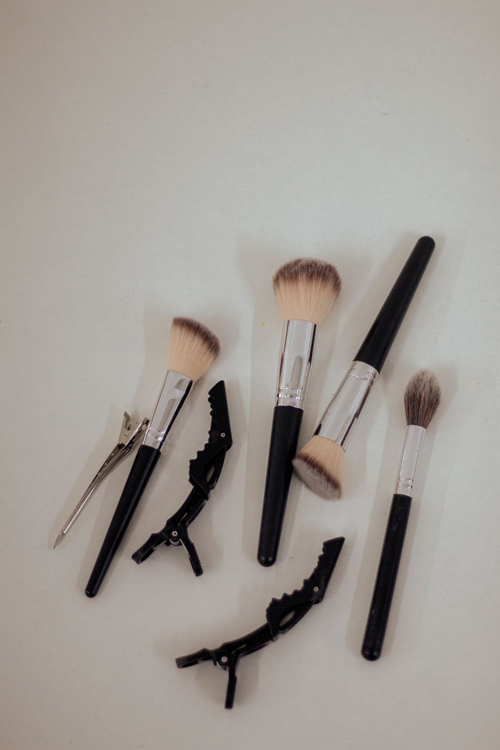 Collection of professional makeup brushes and hair clips arranged on white surface.