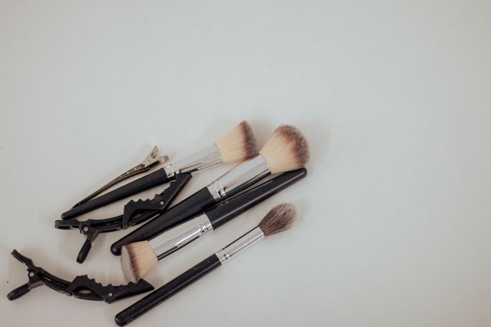 Makeup brushes and hair clips scattered on a white surface with neutral tones.