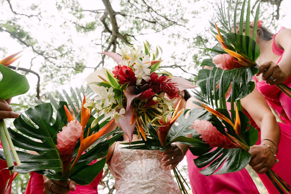 Tropical floral wedding arch decoration with red and pink flowers against natural outdoor backdrop.