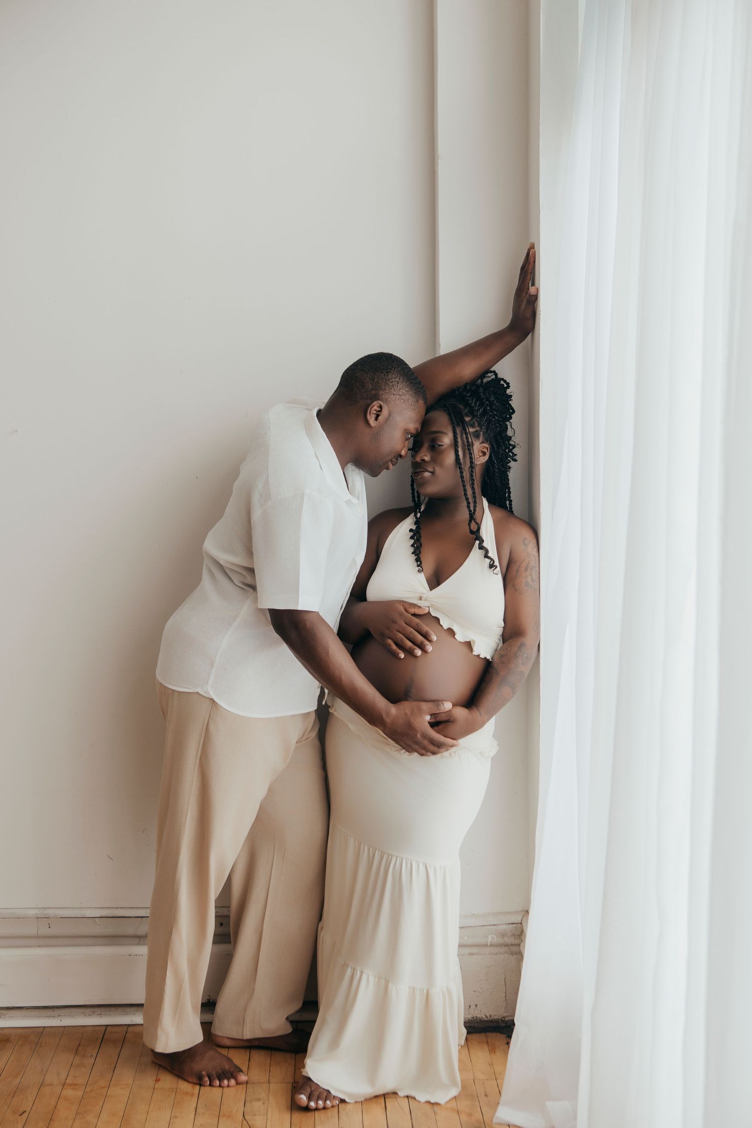 Artistic maternity photo series showing couple in white and beige outfits against neutral wall.