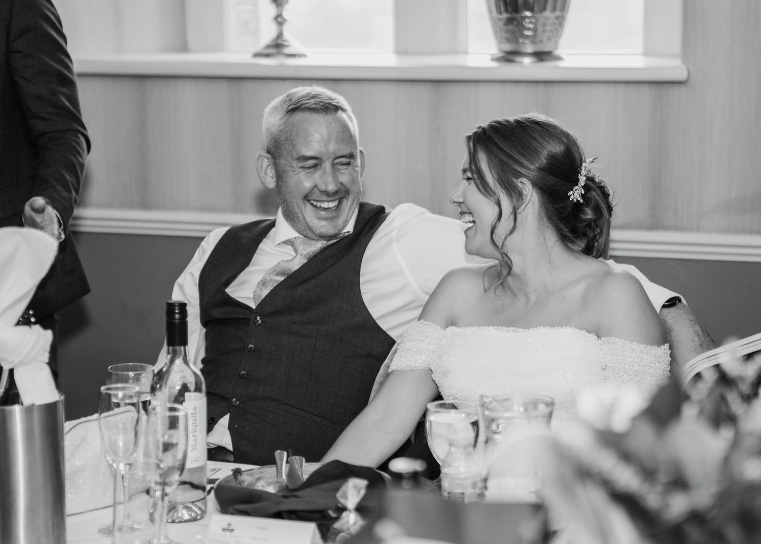 Couple laugh together at the top table whilst listening to speeches.