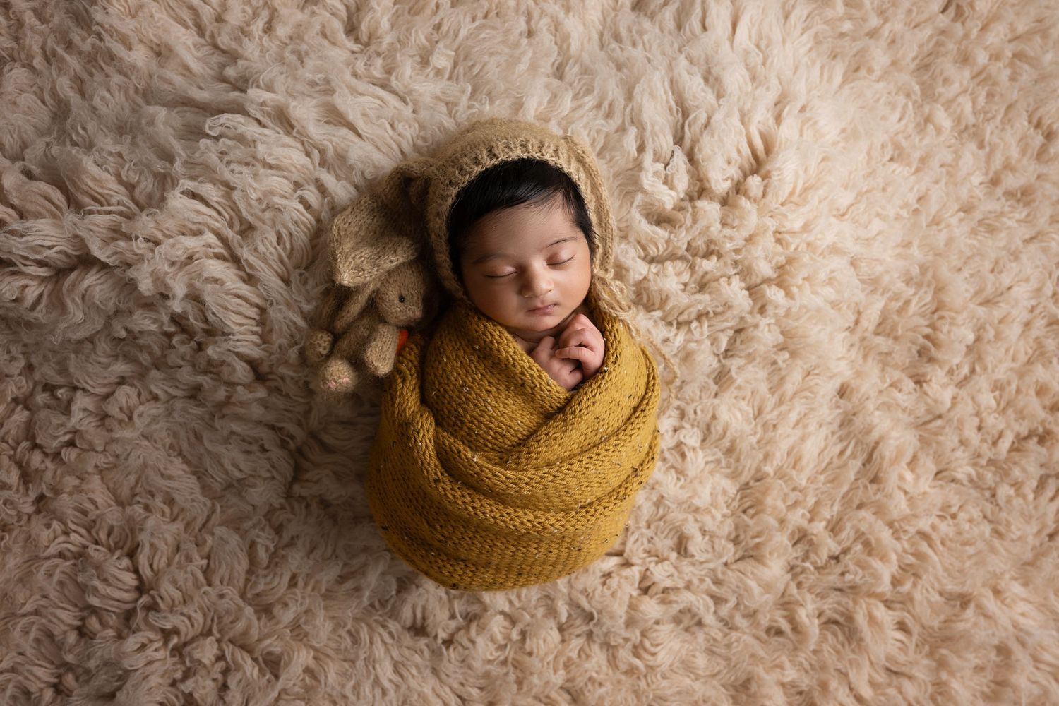 A series of seven cozy newborn photography shots featuring soft beige textures and warm mustard yellow knit accessories.