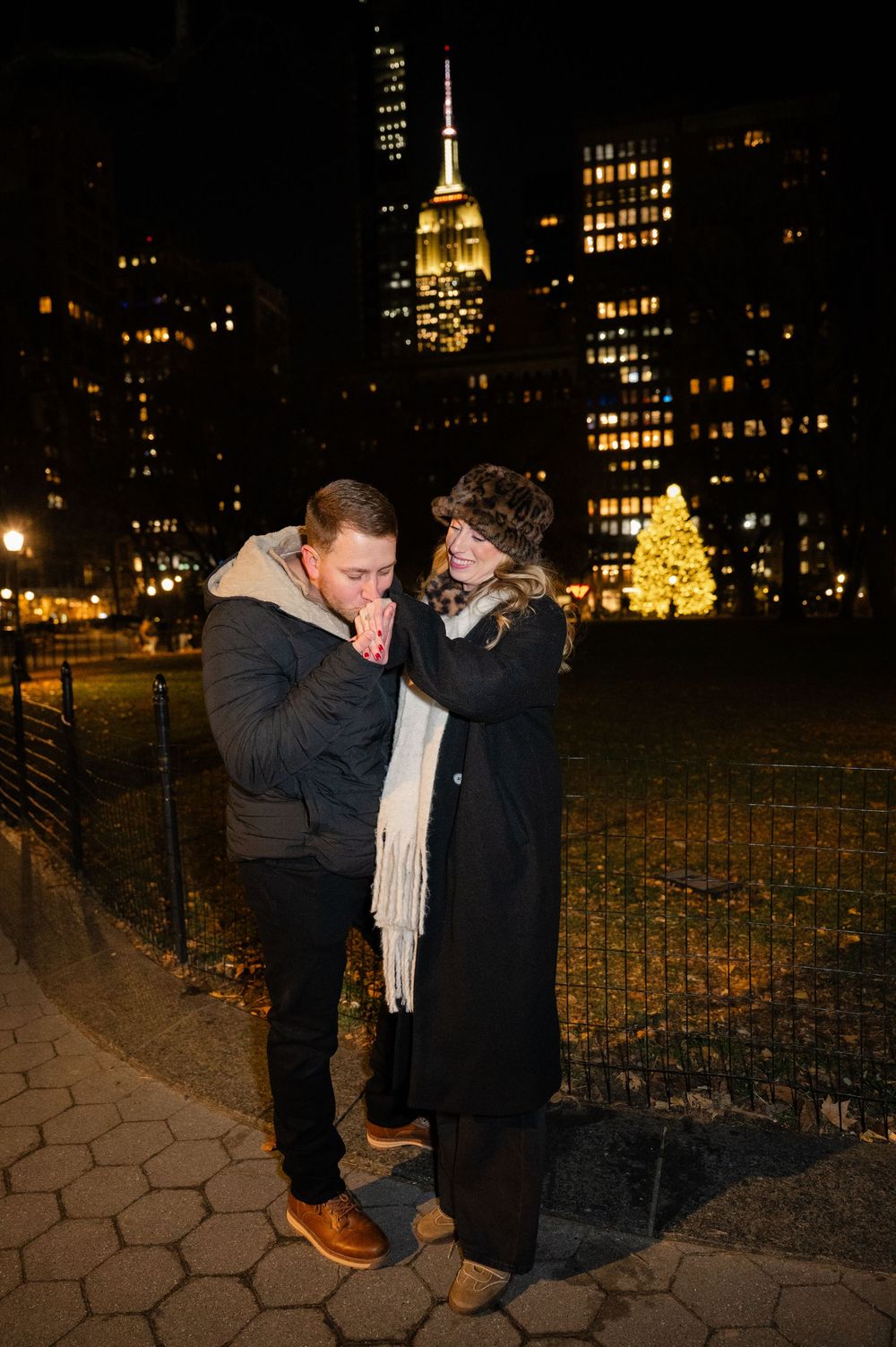 A romantic nighttime proposal scene in New York City with the Empire State Building glowing in the background.