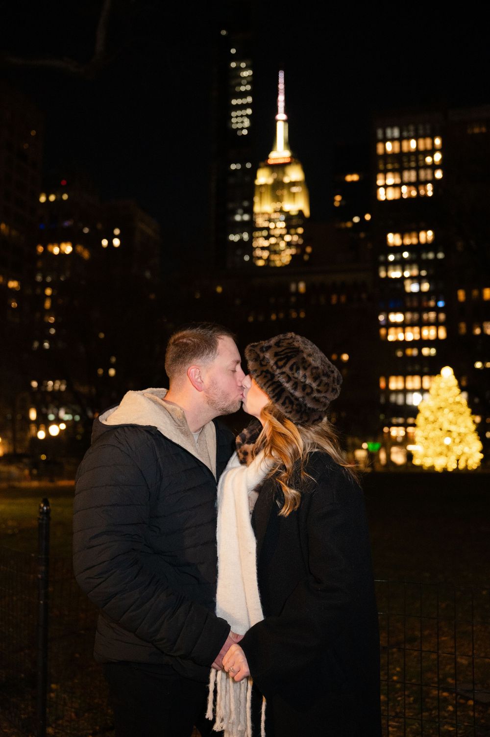 A couple kisses during their engagement session in Madison Square Park with the Empire State building in the backdrop.