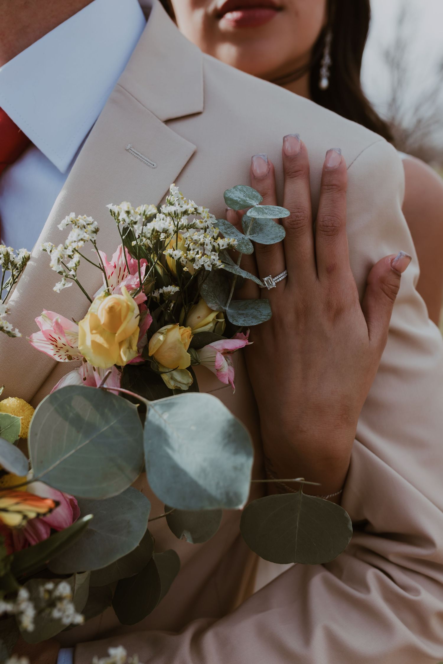 Close-up of bride holding colorful wedding bouquet with eucalyptus, showing elegant engagement ring on her hand.