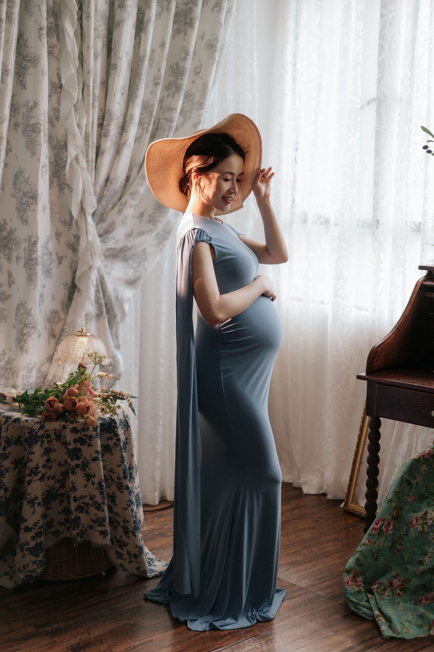 A baby in a brown romper sits next to a decorated cake with sunflowers and white lettering for a milestone celebration.