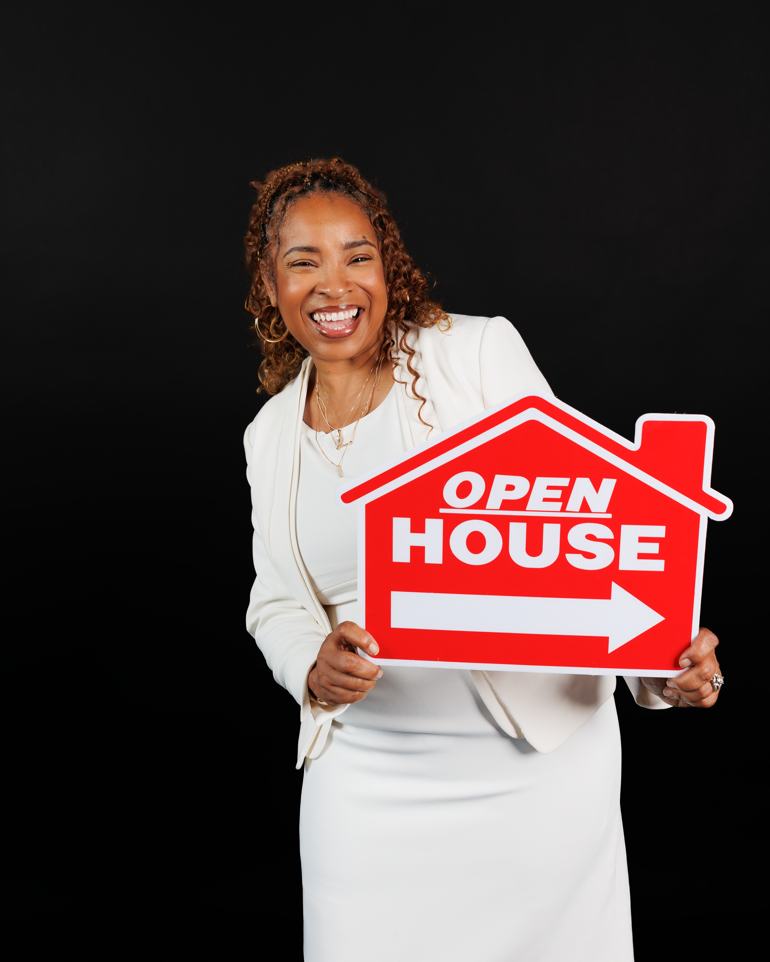 Real estate agent in white top holds red open house directional signs against black background.