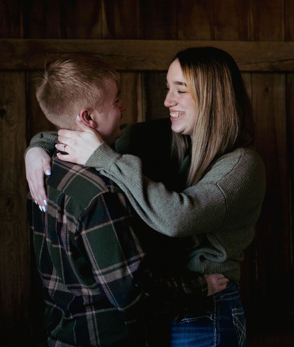 Young couple embracing and smiling together inside rustic wooden barn interior.