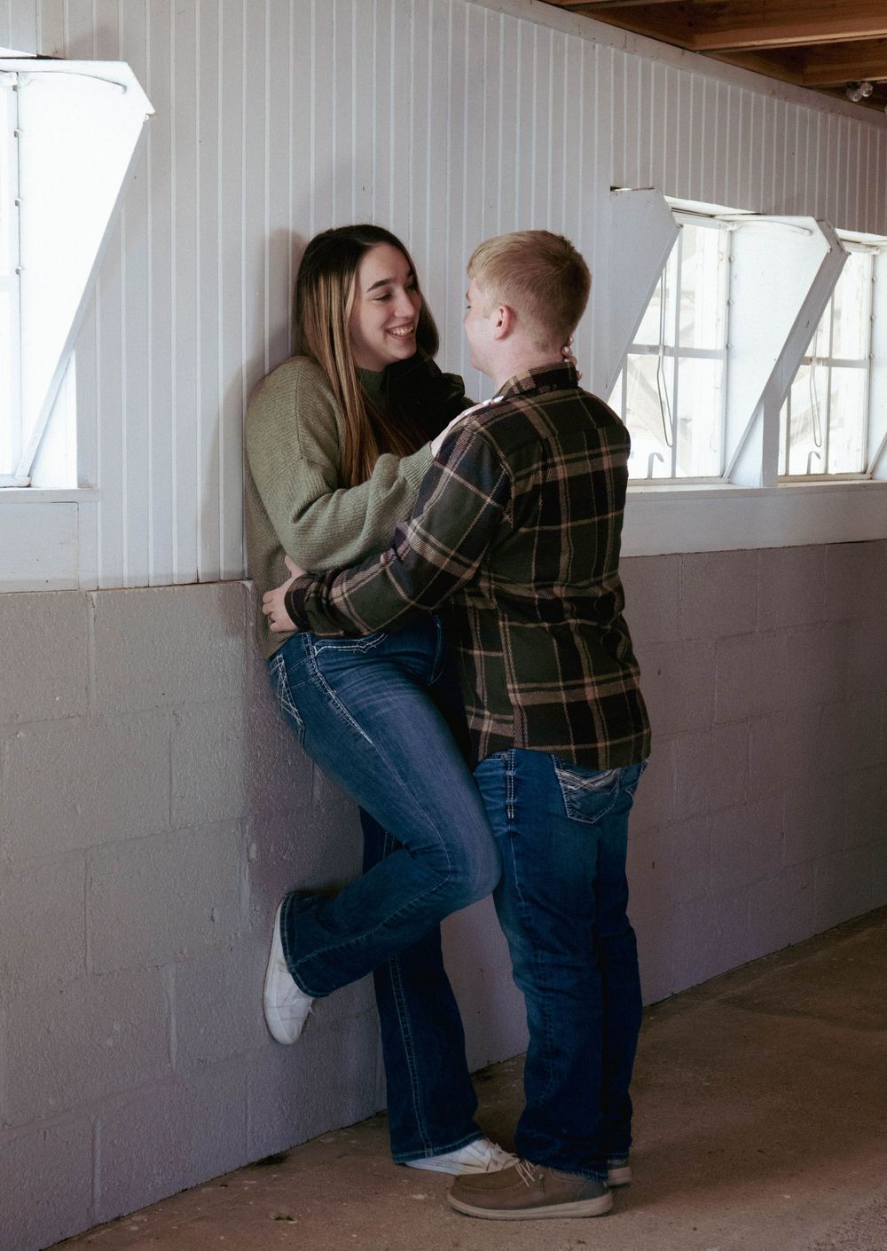 Young couple sharing a romantic moment leaning against a white wall inside a barn.