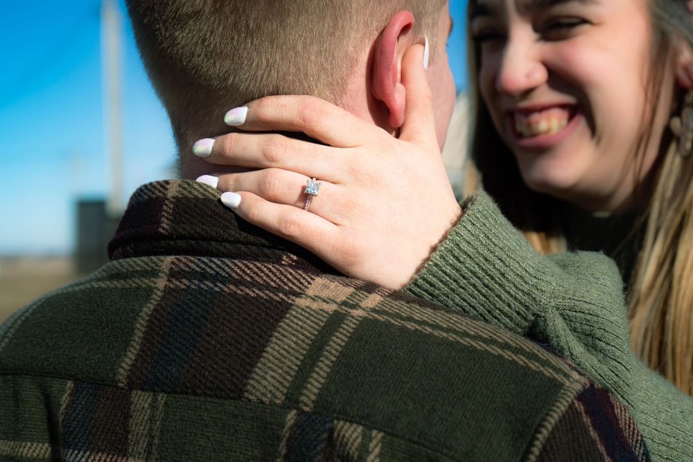 Close-up of womans hand with engagement ring resting on mans neck during outdoor photo.