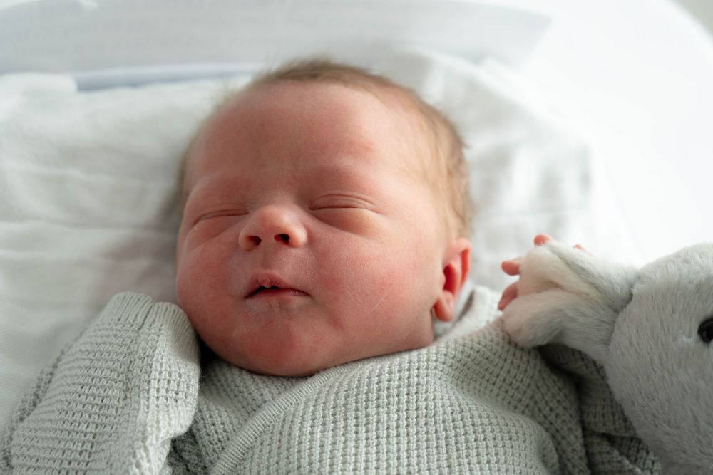 Serene newborn baby sleeping wrapped in a soft green knit blanket in a hospital bassinet.