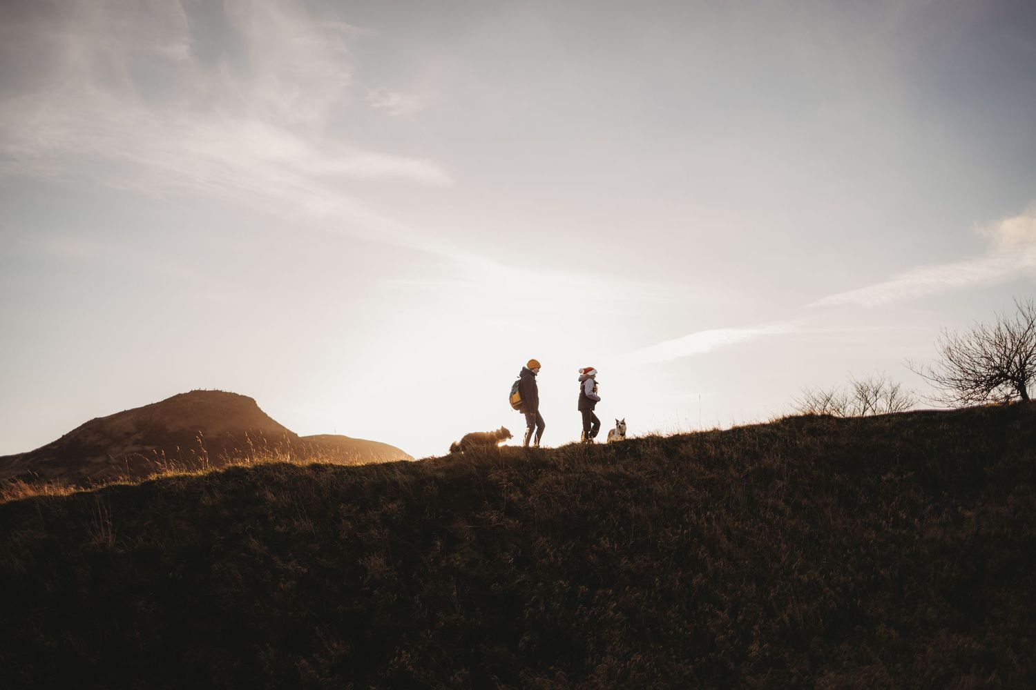 Two silhouetted figures stand on a hilltop ridge against a dramatic sunset sky.
