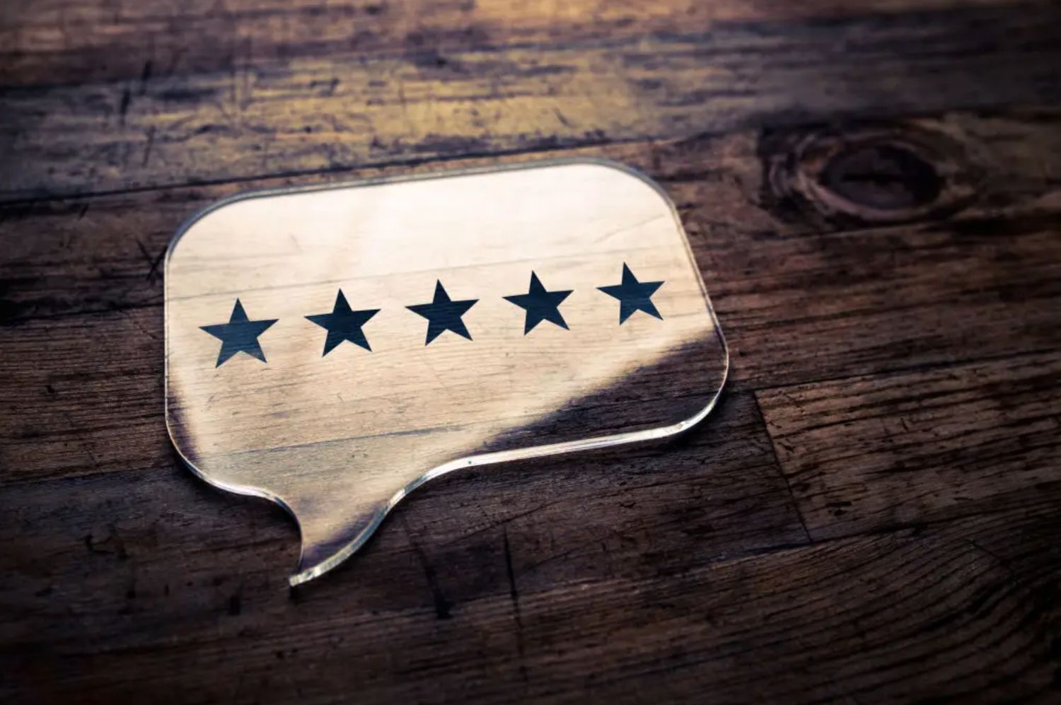 A wooden speech bubble with five star rating displayed on rustic wooden surface.