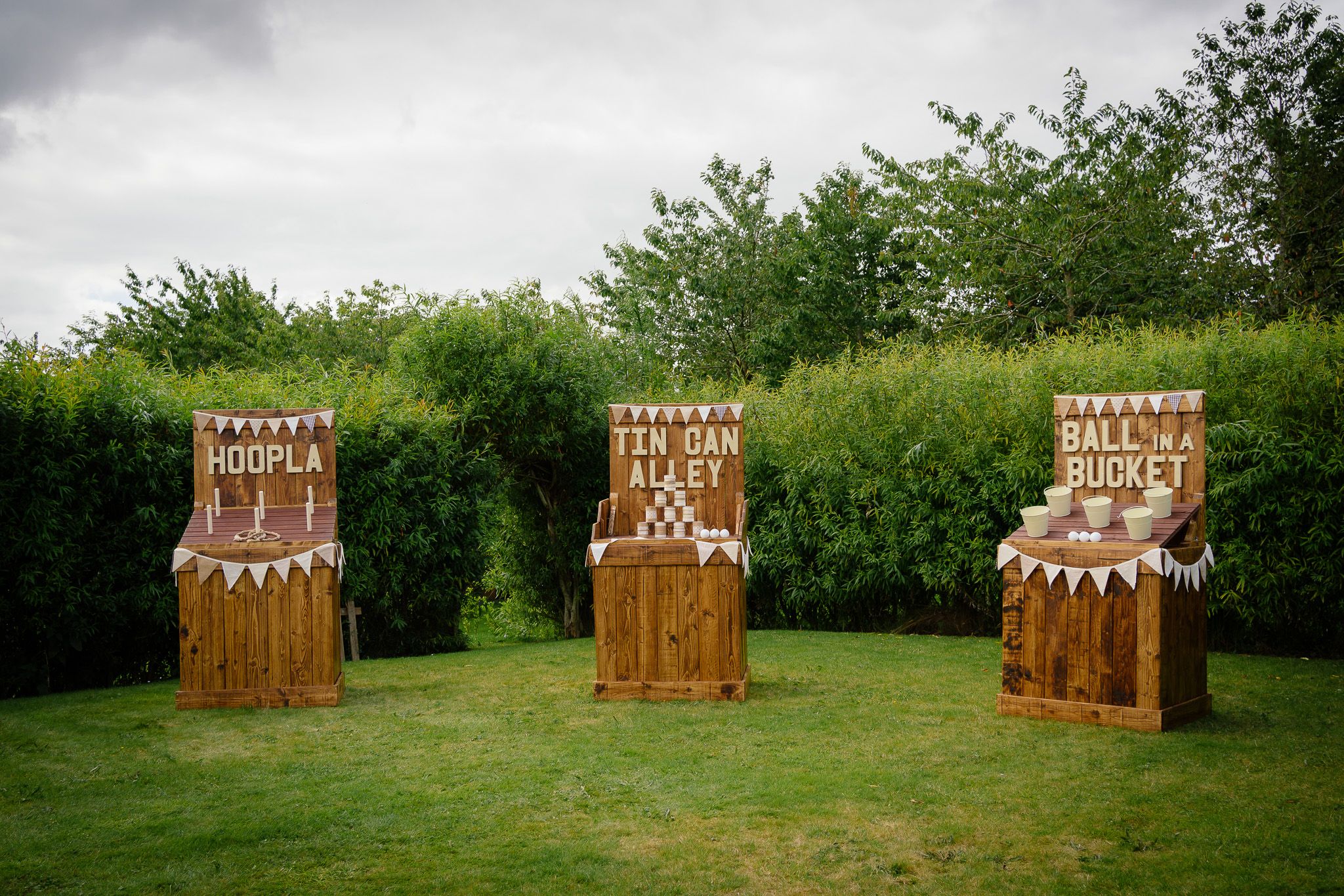 Three rustic wooden chairs decorated with white bunting and lace stand on a green lawn against a hedge backdrop.