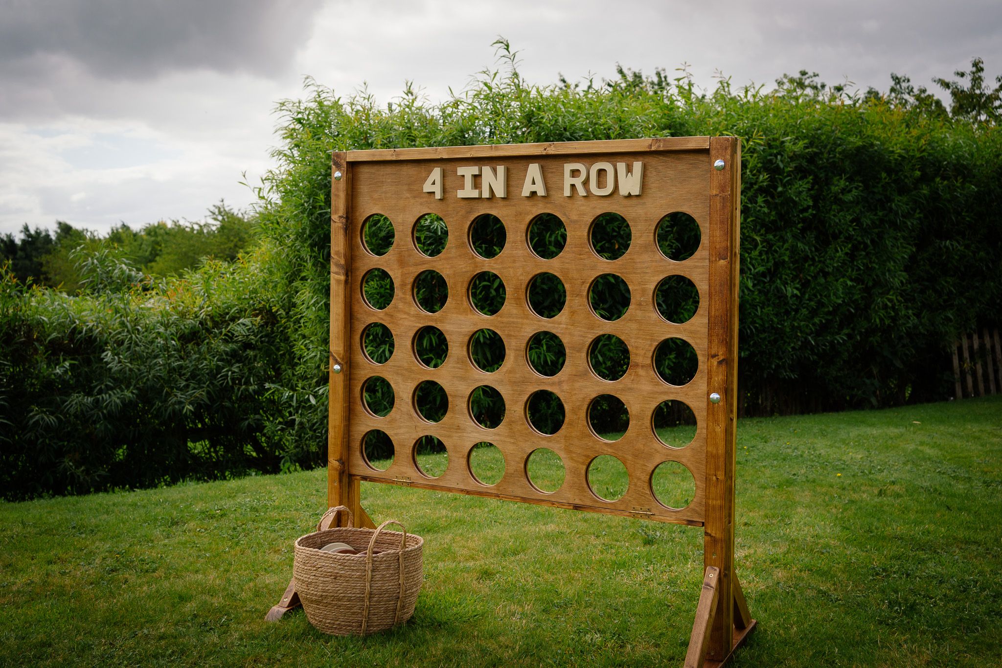 A wooden carnival game board with circular holes for tossing balls sits in a grassy outdoor setting.