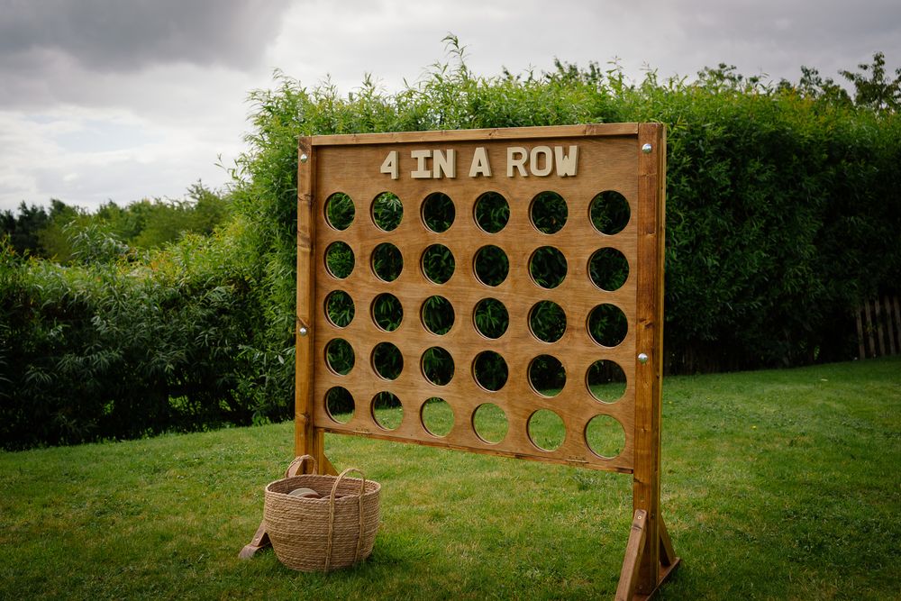 A wooden carnival game board with circular holes for tossing balls sits in a grassy outdoor setting.